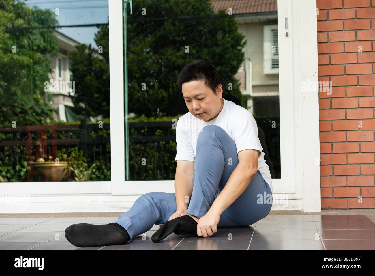 Préparation matinale à la porte, il est assis près du patio et met des chaussettes avant de partir. Un départ calme et organisé qui donne le ton pour la journée. Banque D'Images