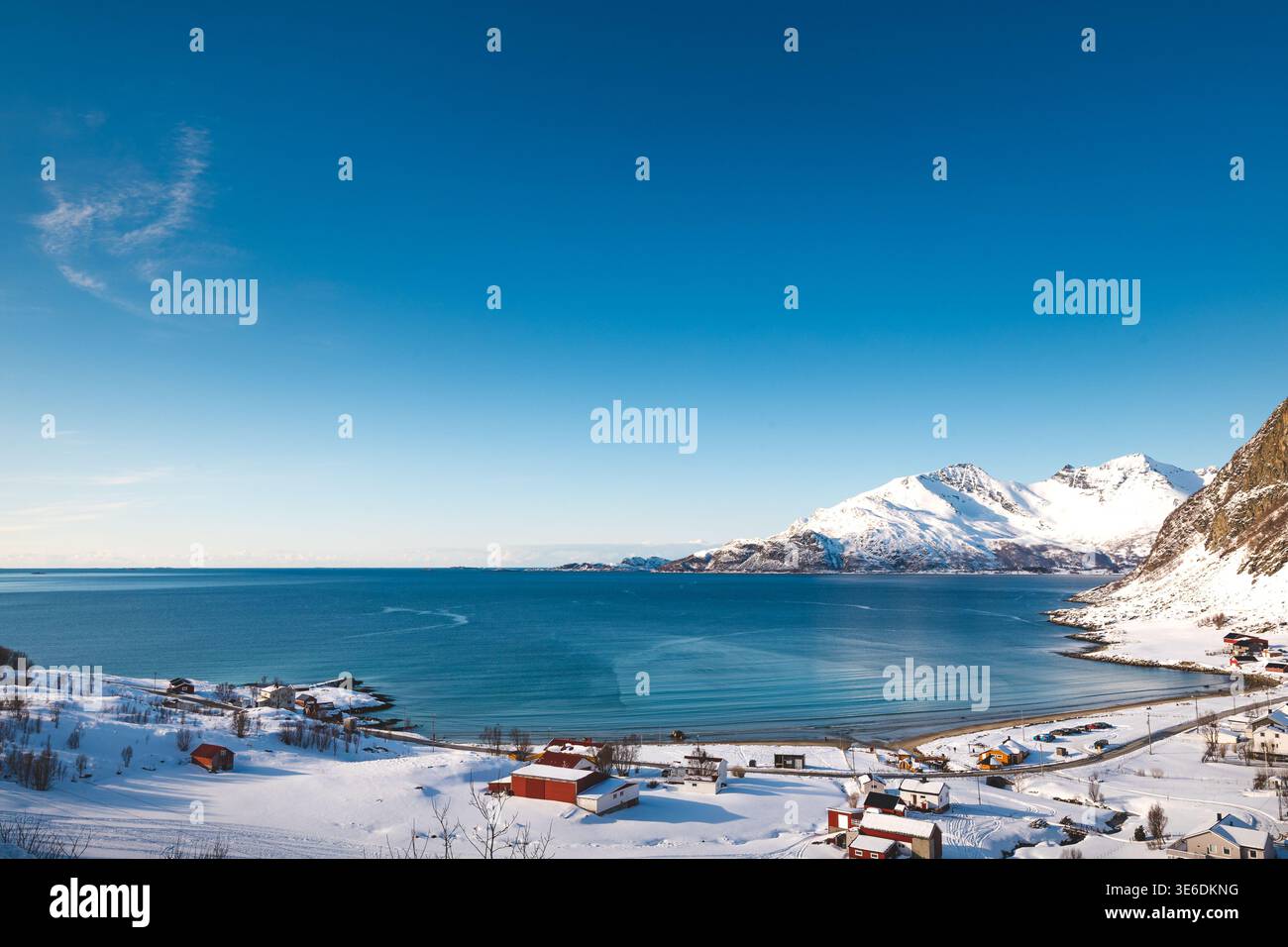 Vue aérienne d'un petit village côtier sur l'île de Kvaloya, en Norvège, entouré de montagnes enneigées et d'un fjord arctique calme sous un ciel hivernal clair Banque D'Images
