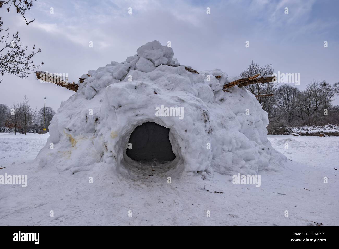 Structure d'igloo simple avec trou d'entrée en saison hivernale, faite pour le plaisir de la neige et des bûches en bois pour le support de toit dans le parc urbain. Banque D'Images