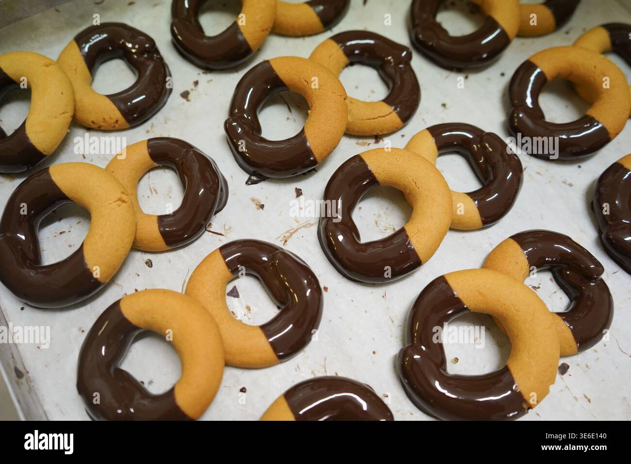 Biscuits crétois gourmands partiellement trempés dans du chocolat noir, disposés sur du papier parchemin pour apporter une touche de modernité aux pâtisseries grecques traditionnelles. Banque D'Images