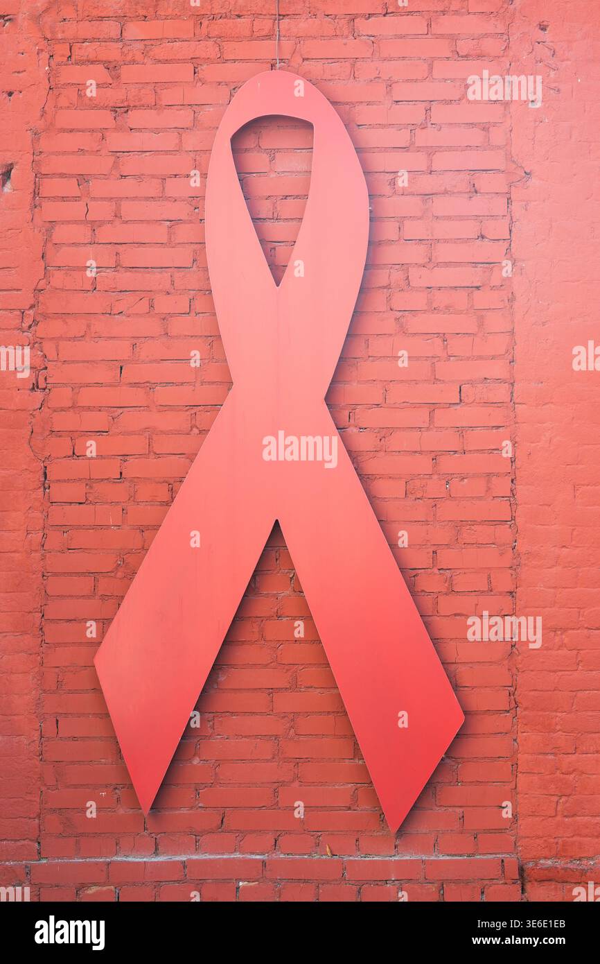 Symbole de sensibilisation au VIH et au sida. Ruban rouge sur un fond de briques peintes rouges. Grand ruban rouge sur un mur de briques. Concept de la Journée mondiale de lutte contre le sida Banque D'Images