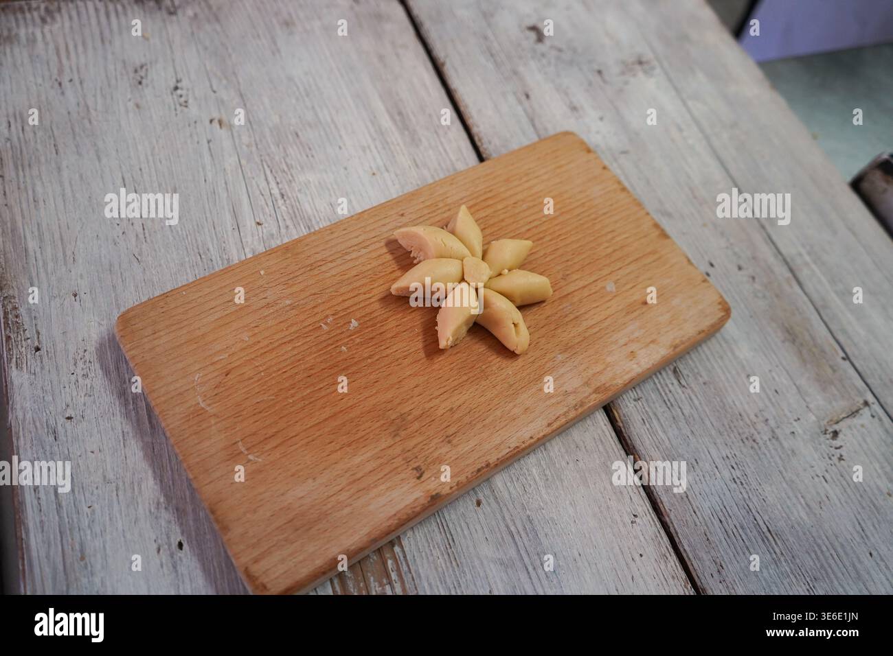 Pâte crétoise faite à la main façonnée en une fleur étoilée traditionnelle sur une planche de bois, mettant en valeur l'authentique savoir-faire méditerranéen de la cuisson. Banque D'Images