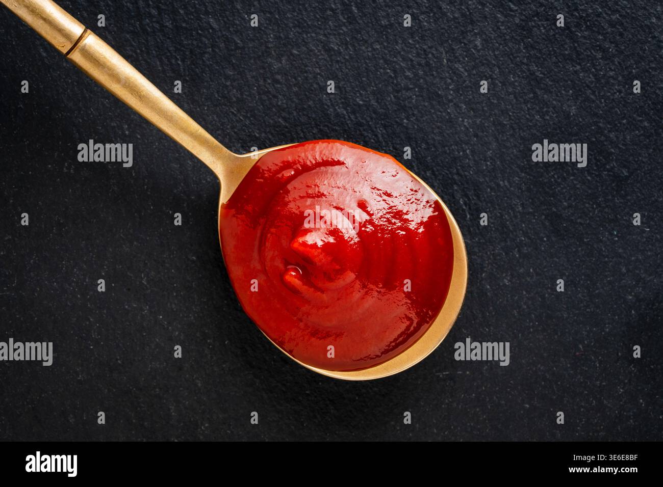 Gros plan de ketchup tomate brillant sur une cuillère sur fond texturé foncé composition minimale idéale pour la conception de menu de publicité alimentaire et condiment br Banque D'Images