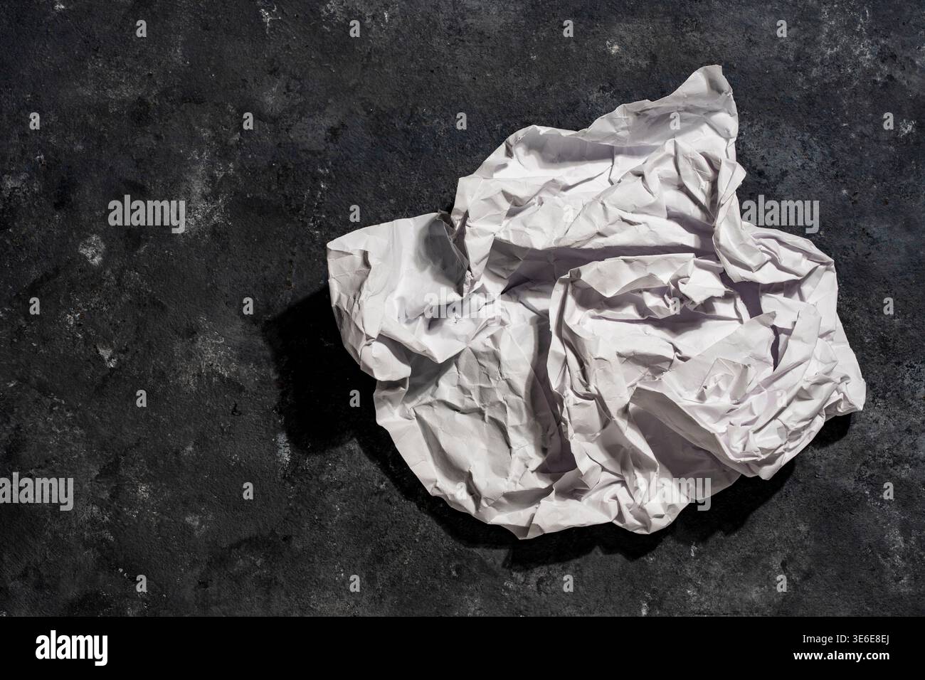 Une boule de papier blanc froissé sur une surface texturée en béton noir. Symbolique d'idées ratées, de déchets, de recyclage ou d'un nouveau départ dans l'entreprise créative Banque D'Images