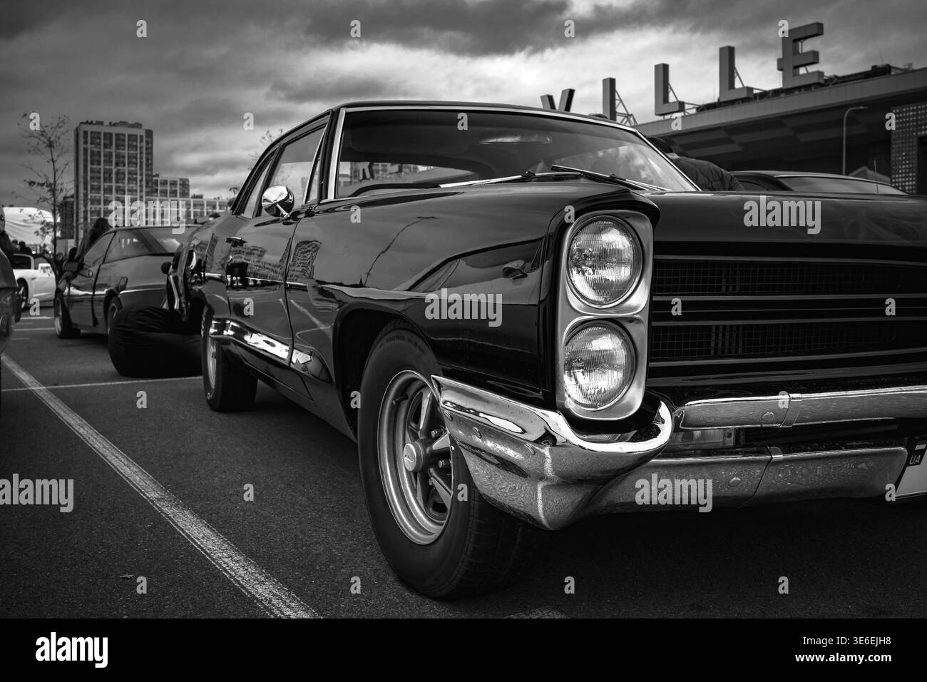 Photographie noir et blanc à angle bas d'une Pontiac Catalina classique garée lors d'un événement automobile extérieur. Le traitement monochrome Moody souligne le chrome Banque D'Images