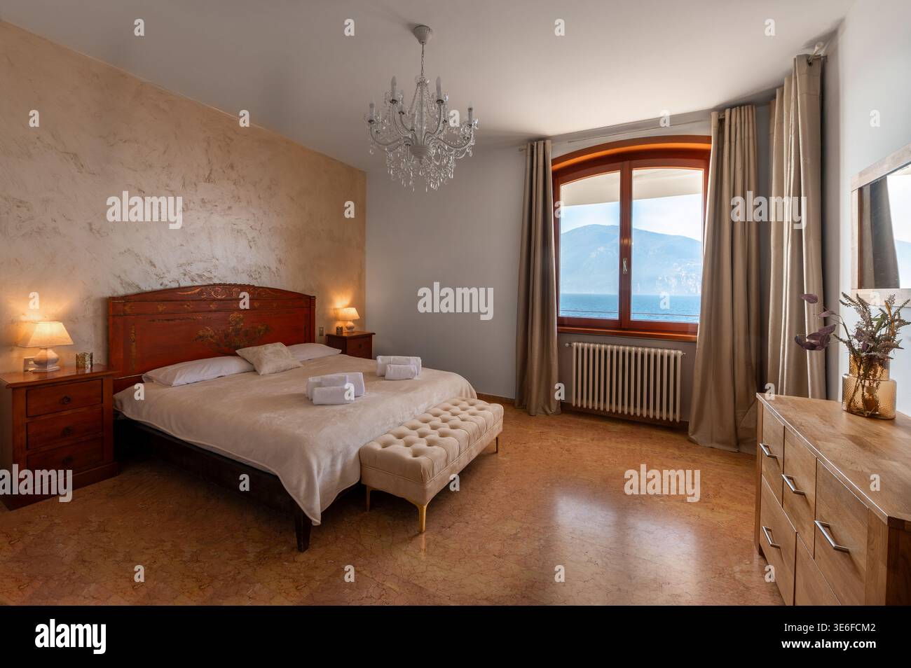 Chambre élégante dans une villa de luxe donnant sur une propriété italienne au bord du lac, avec lit king size, lustre, meubles en bois chaleureux et une montagne sereine Banque D'Images