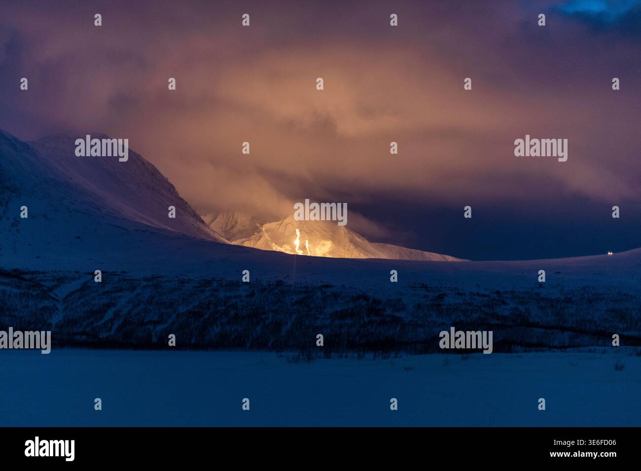 Scène nocturne hivernale spectaculaire près de Tromso, en Norvège, avec des montagnes enneigées et une vallée sous de lourds nuages, une lumière brillante à l'horizon dans Arctic Lap Banque D'Images