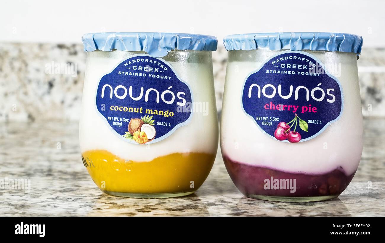 NORWALK, CT, États-Unis - 25 NOVEMBRE 2024 : deux pots de yogourt grec Nounos avec de la mangue de noix de coco et de la tarte aux cerises se trouve sur un comptoir en granit lisse, highligh Banque D'Images
