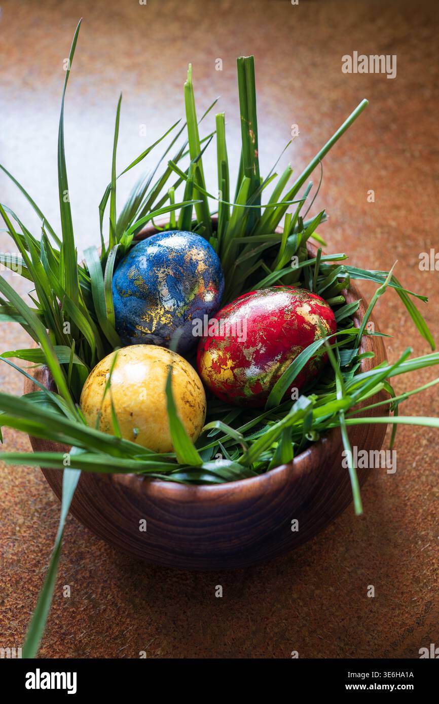 Trois oeufs de pâques peints à la main colorés avec du papier d'or dans un bol en bois rempli d'herbe verte. Vue de haut en bas, lumière naturelle de la fenêtre, pas de gens Banque D'Images