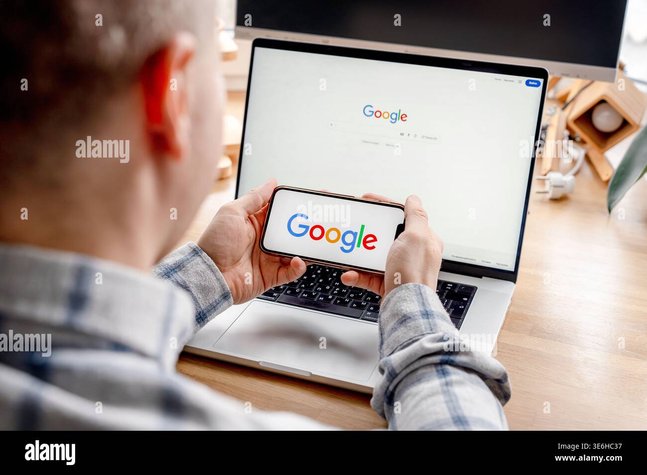 Un homme tient un smartphone avec une application Google et un ordinateur portable ouvert avec un site de recherche. Saint-Pétersbourg, Russie - 7 avril 2026 Banque D'Images