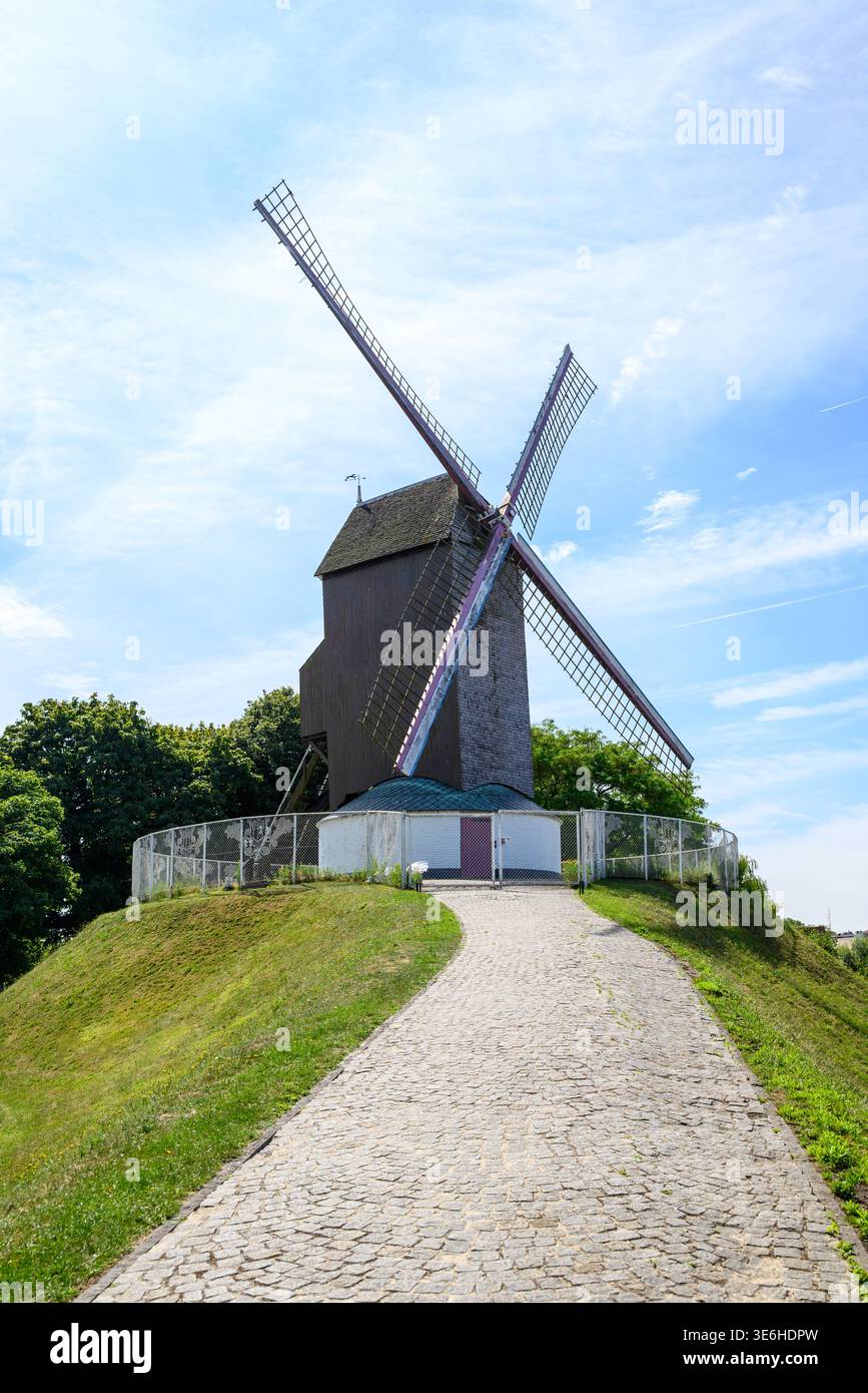 Moulin à vent traditionnel en bois sur une colline herbeuse, vu d'un chemin pavé sous un ciel bleu vif avec des nuages légers ; repère rural et voyage Concepp Banque D'Images