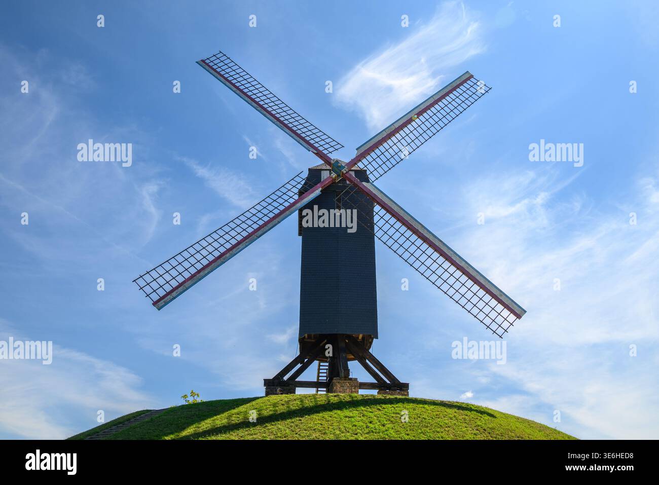 Moulin à vent traditionnel en bois avec quatre voiles en treillis sur une colline herbeuse sous un ciel bleu vif avec des nuages sinueux, vue à angle bas, paysage rural, journée ensoleillée Banque D'Images