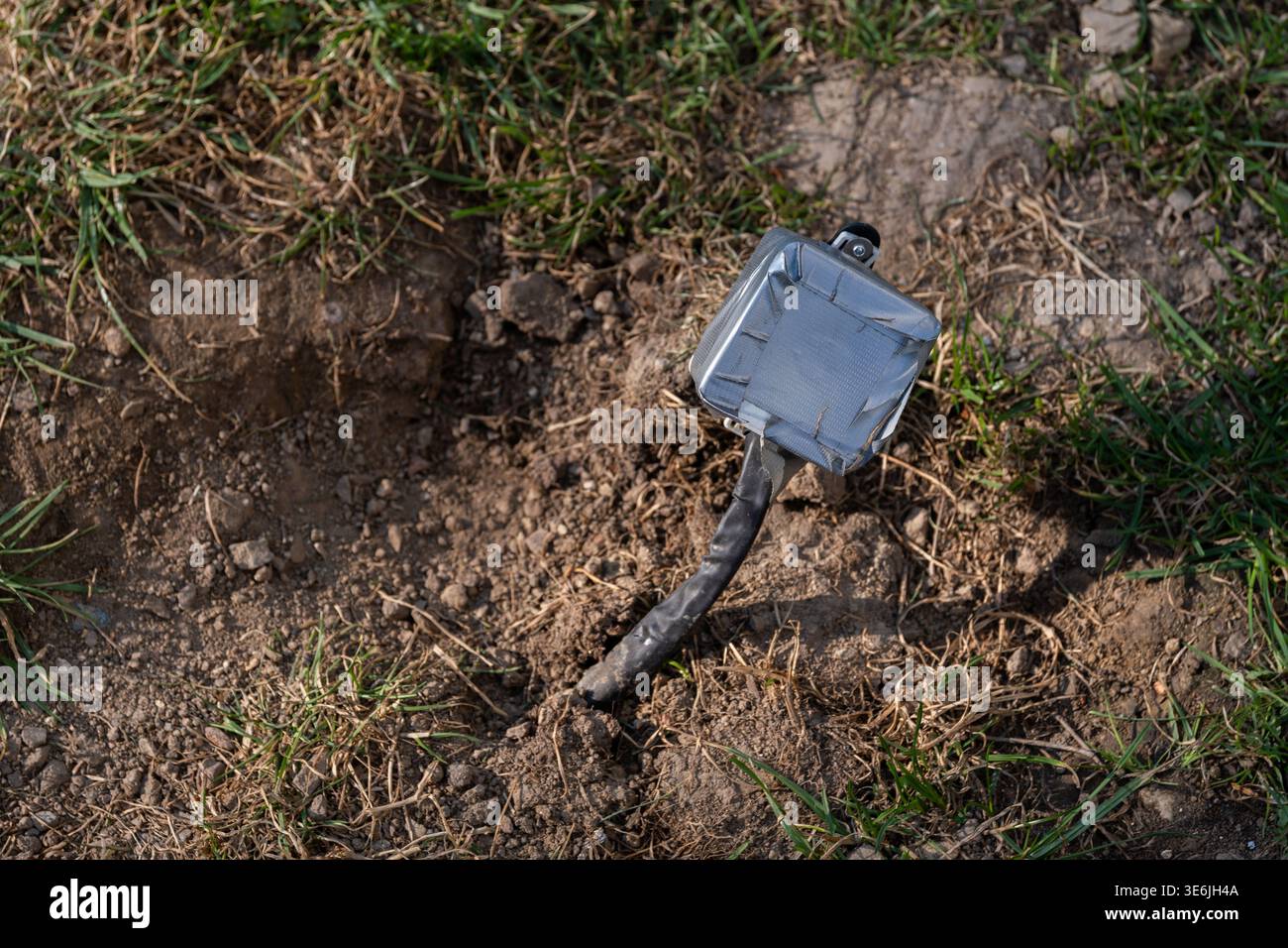 Vue rapprochée d'une boîte de jonction électrique exposée avec un câble sortant du sol dans un environnement extérieur. Concept de danger électrique, câblage dangereux, et Banque D'Images