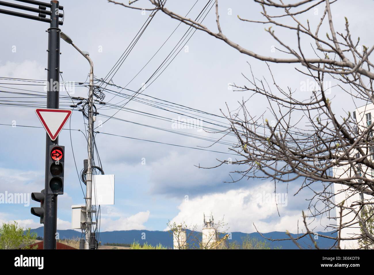 Feu de signalisation rouge flèche contre un ciel nuageux avec des fils électriques denses et des infrastructures urbaines Banque D'Images