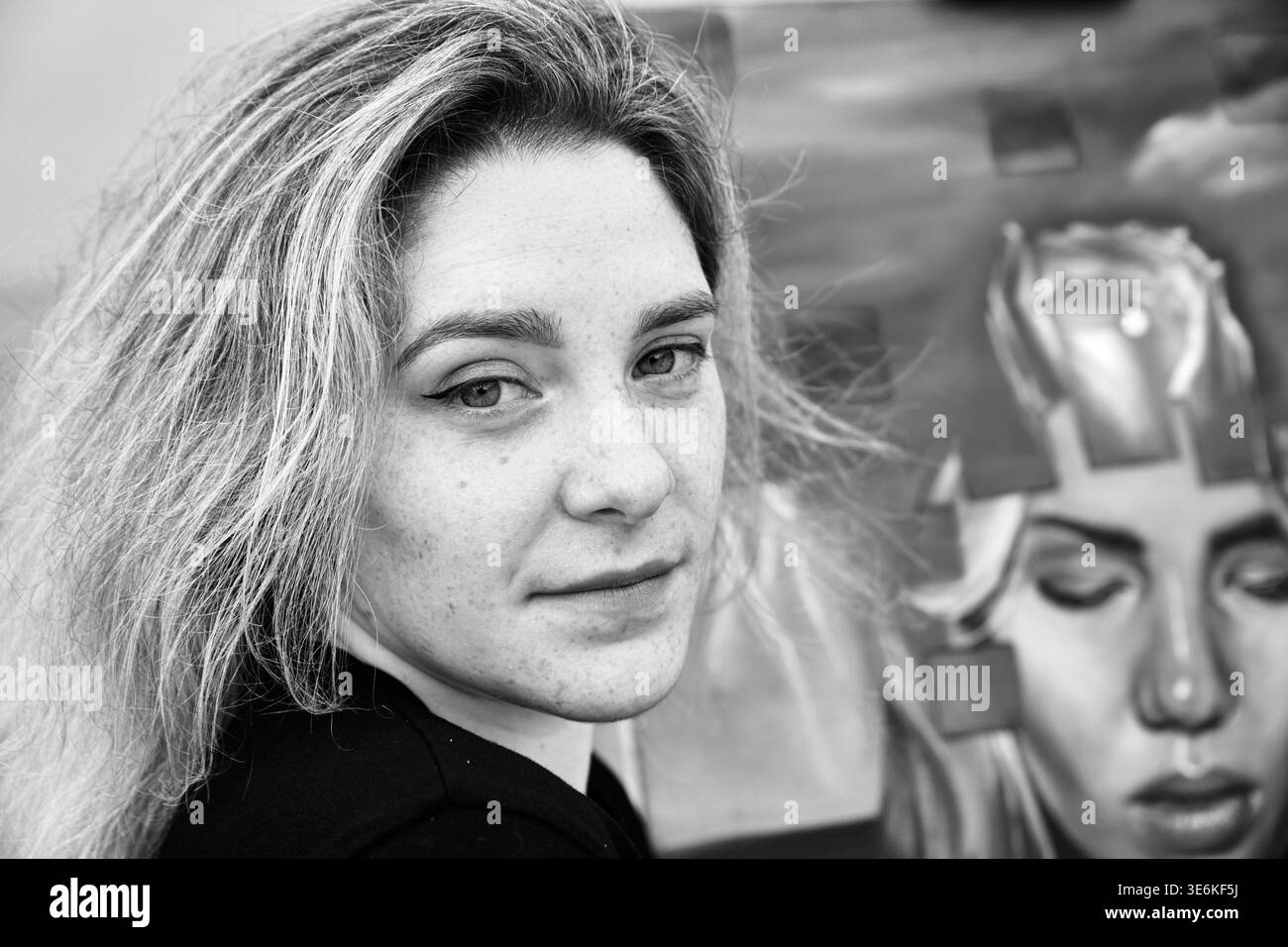 Artiste féminine adulte avec la peau claire et les taches de rousseur se tient calmement à côté de sa grande peinture abstraite dans un environnement de studio légèrement éclairé. Expression suggérer Banque D'Images