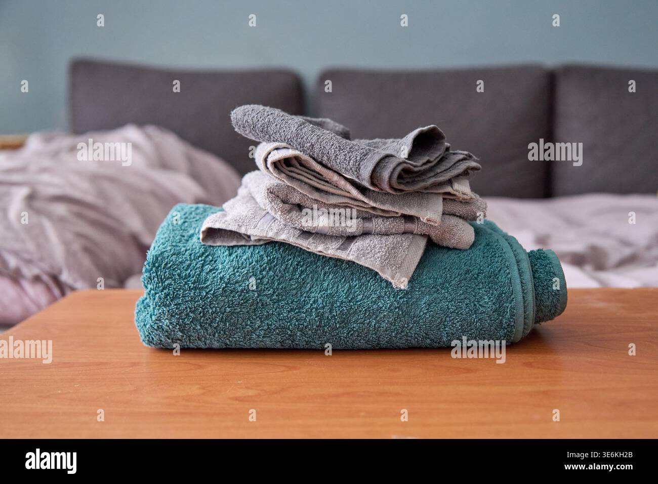 Serviette turquoise en peluche avec de petites serviettes grises et beiges soigneusement pliées empilées sur le dessus, placées sur une surface en bois chaude dans le cadre du salon avec sourdine Banque D'Images