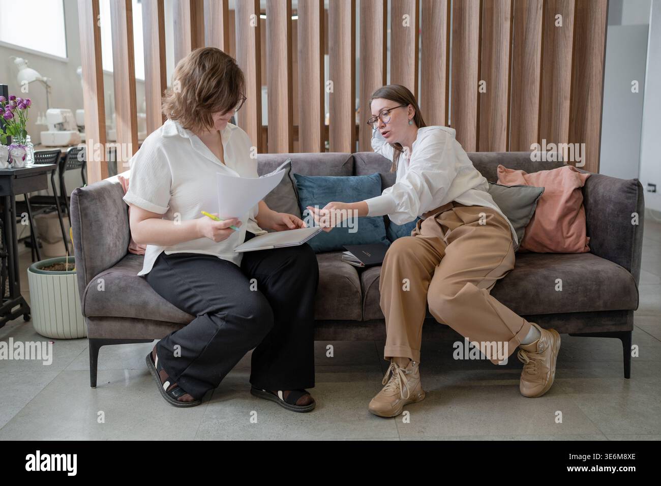 Deux femmes assis à proximité et analysant des documents sur le canapé ensemble dans le bureau moderne de l'entreprise. Analyse, documents, femmes, canapé, moderne, affaires. Banque D'Images