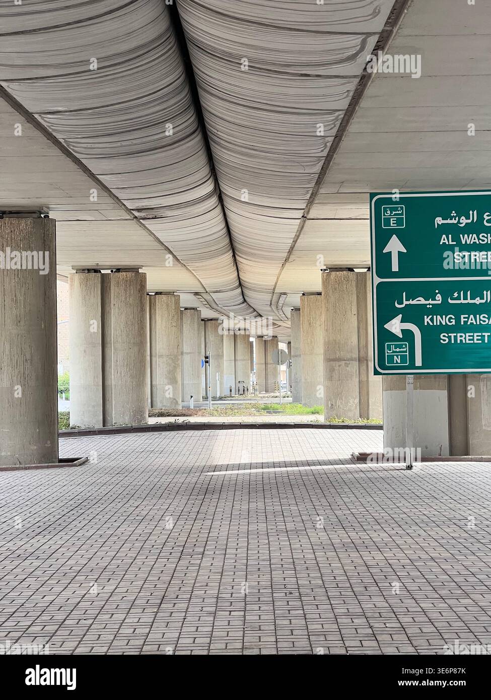 Espace pavé vide sous une chaussée surélevée avec des panneaux de direction bilingues à Riyad, Arabie Saoudite. - Image de stock capturée avec un smartphone