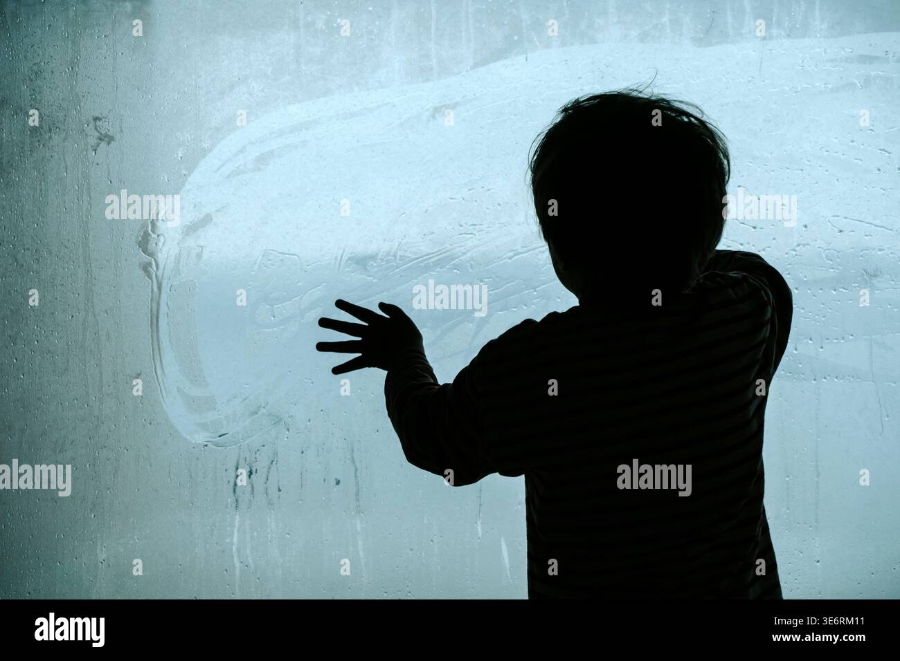 Silhouette d'un enfant solitaire regardant à travers une grande fenêtre embuée froide. Un travail de photographie conceptuelle explorant les thèmes de la dépression infantile, de la crise psychologique et du profond sentiment d’isolement et de tristesse. Photo de haute qualité Banque D'Images