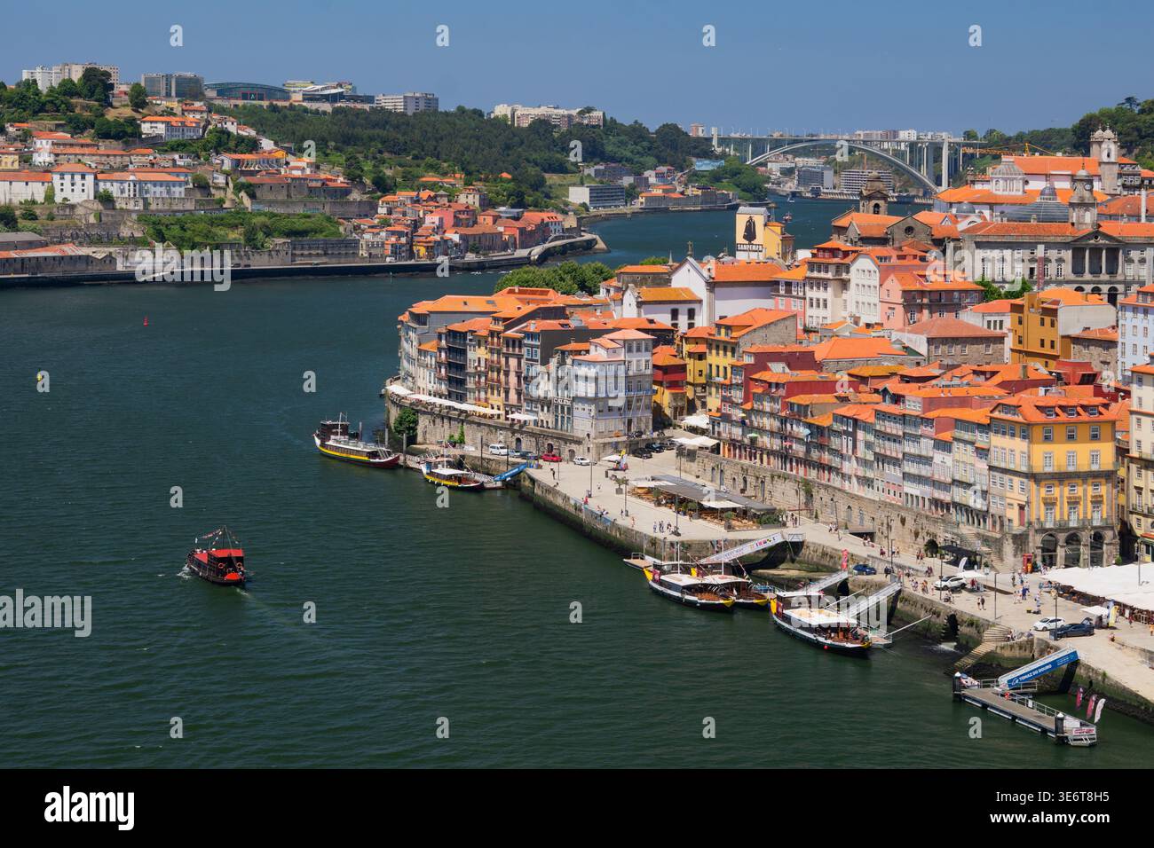 Vue aérienne du fleuve Douro serpentant à travers la ville, bordée de bâtiments colorés et de bateaux, sous un vaste ciel, Porto, Porto District, Portugal. Banque D'Images