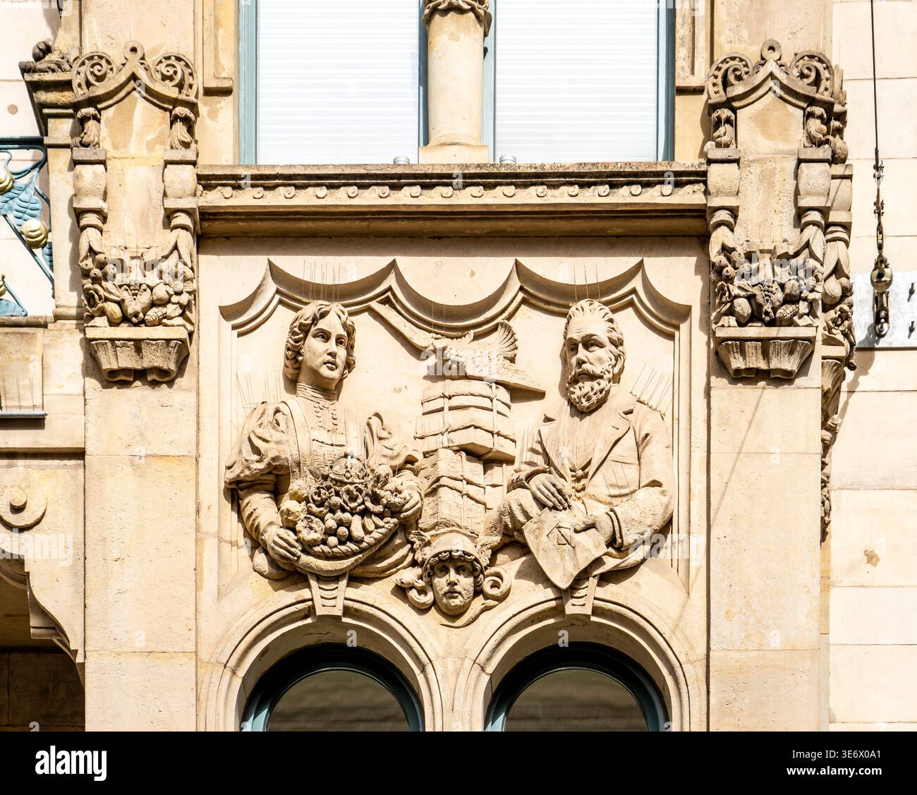 Bas-relief en pierre orné sur une façade de bâtiment représentant une femme tenant un panier de fruits, un homme barbu avec des livres, ornement architectural ci-dessus Banque D'Images