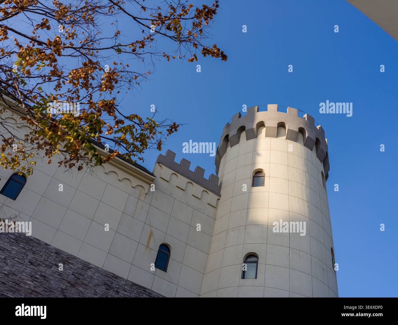 Vue en bas angle d'une tour ronde classique de style château blanc avec créneaux, partiellement encadrée par des branches d'arbres d'automne sous un ciel bleu clair. Le SC Banque D'Images