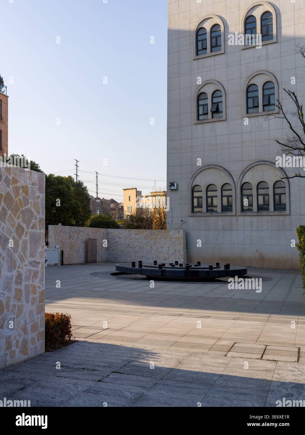 Une cour pavée vide avec une fontaine circulaire sombre au centre, située en face d'un château blanc de style européen avec une arche Banque D'Images
