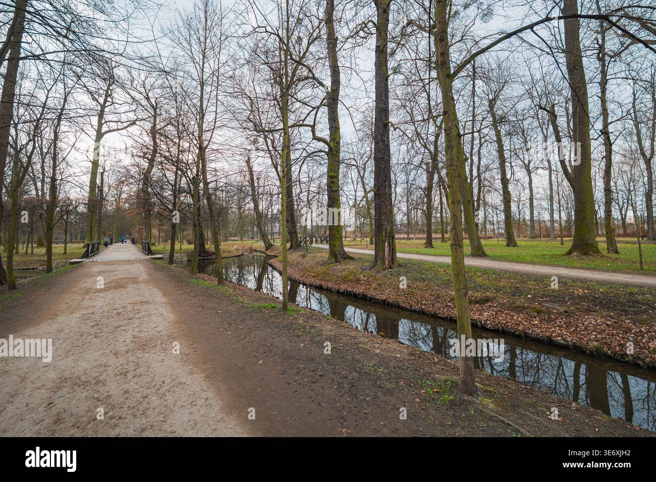 Pittoresque chemin de gravier serpentant à travers un parc urbain vert à côté d'une aire de loisirs Calm River Riverside avec des arbres luxuriants et des reflets naturels Banque D'Images