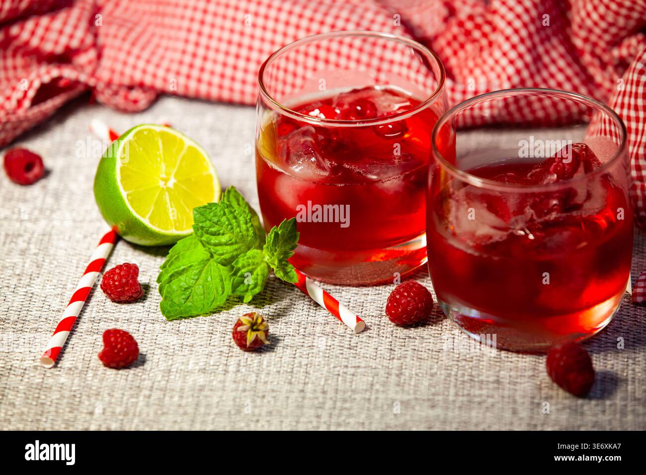 Cocktail d'été rouge froid avec framboises fraîches, glaçons et feuilles de menthe sur un fond rustique. Limonade maison saine avec citron vert et paille, no p Banque D'Images