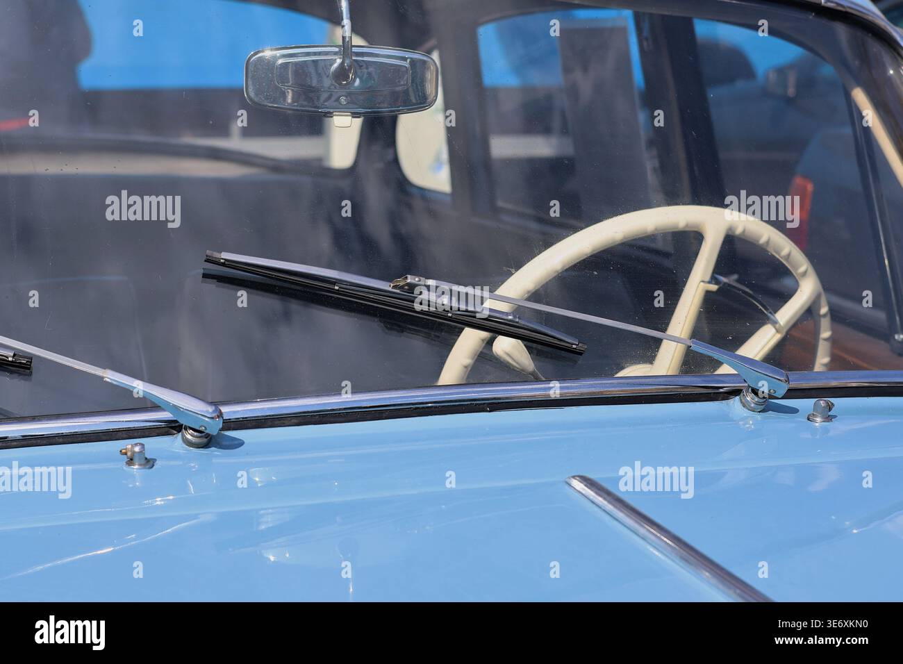 Vue sur le capot bleu d'une voiture vintage à travers le pare-brise vers un volant blanc Banque D'Images