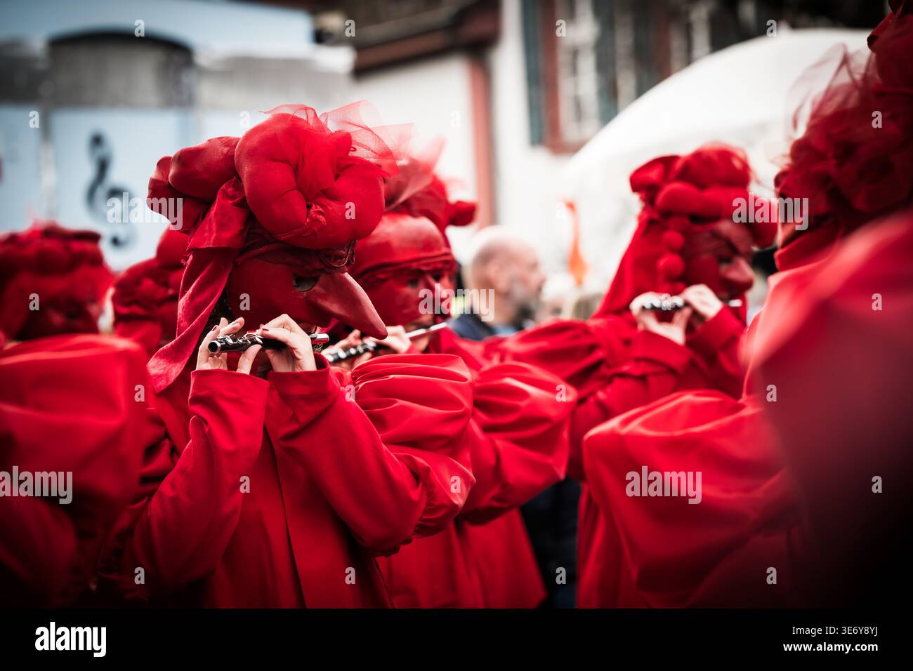 Bâle, Suisse - 10 mars 2025 : vue de personnages habillés de rouge vif, masqués et jouant de flûtes pendant Fasnacht, un éclat de couleur contre le muet ur Banque D'Images
