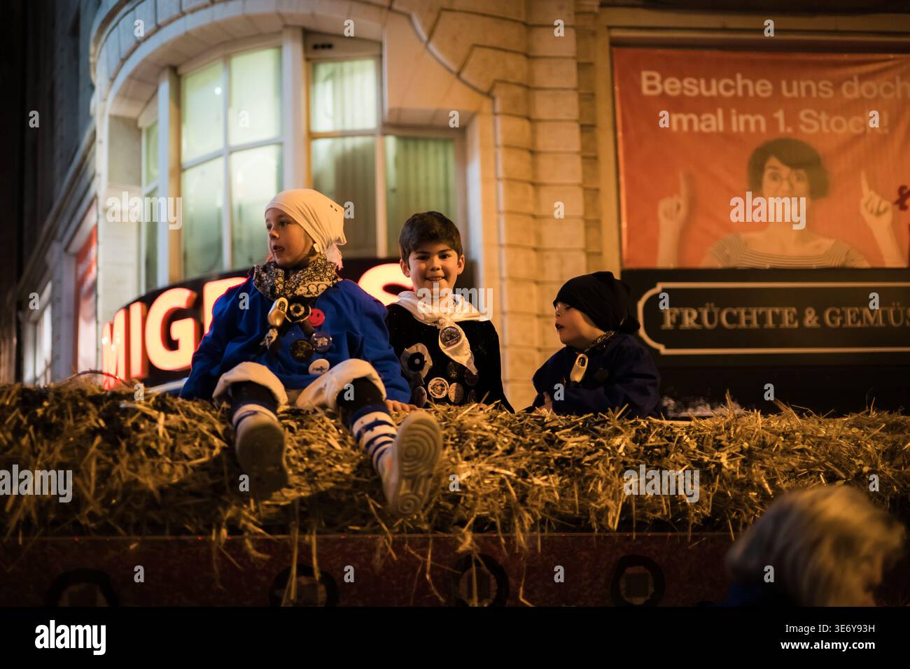 Bâle, Suisse - 10 mars 2025 : vue d'enfants en costumes traditionnels au sommet d'un flotteur couvert de foin, leurs tenues lumineuses contrastent fortement avec le di Banque D'Images