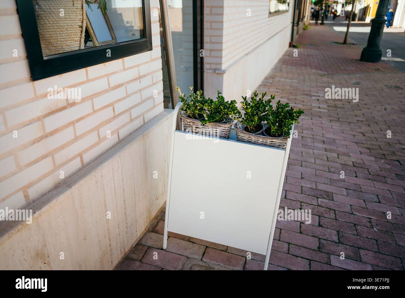 Panneau blanc vierge de panneau sandwich debout sur un trottoir de briques à côté d'un mur de bâtiment Banque D'Images