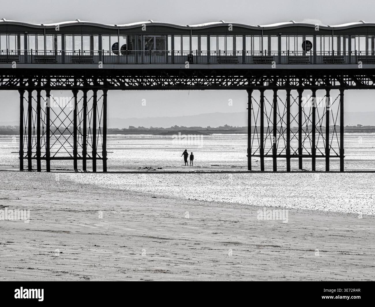 Deux personnages marchant sous le Grand Pier à Weston super Mare à marée basse sur la côte nord du Somerset Royaume-Uni - image monochrome Banque D'Images