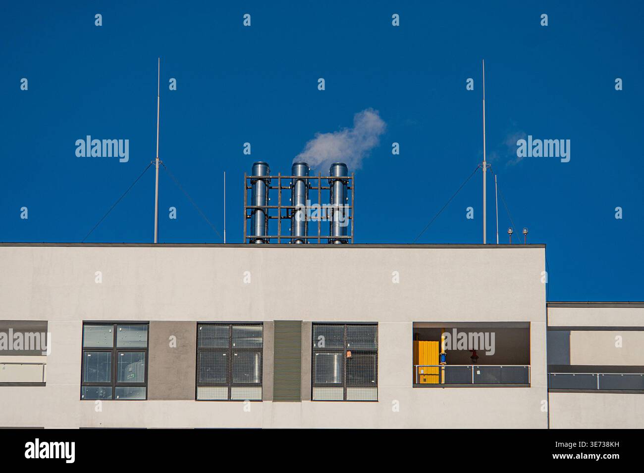 Vue plongeante d'un grand bâtiment industriel blanc avec toit gris, deux cheminées, grue jaune, grandes fenêtres Banque D'Images