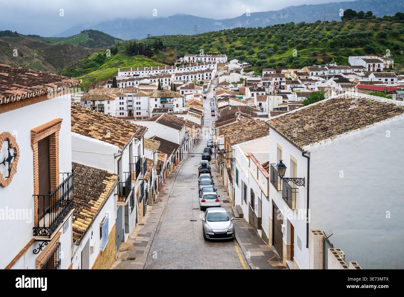 Une perspective à grand angle capture une longue rue pavée à Antequera, bordée de maisons blanchies à la chaux et de toits en terre cuite. Les voitures garées parsèment la route lea Banque D'Images