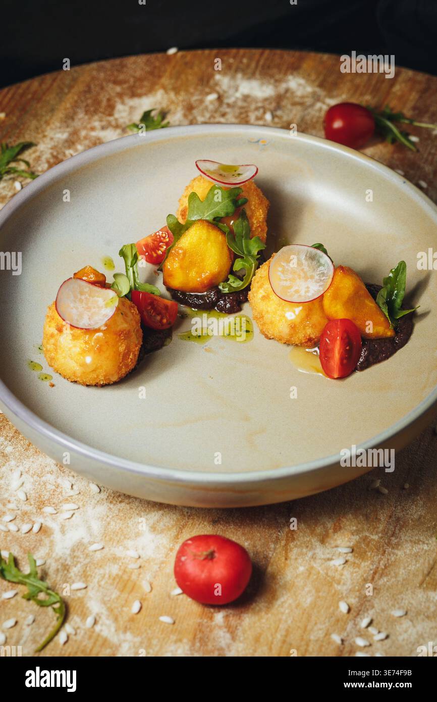 Boules d'arancini frites gourmandes servies avec une sauce salée foncée tomates cerises fraîches et tranches de radis sur une assiette en céramique. Banque D'Images