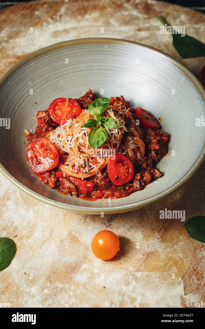 Délicieux spaghetti bolognaise avec une riche sauce à la viande tomates cerises fraîches et fromage parmesan râpé garni de basilic dans un bol en céramique. Banque D'Images