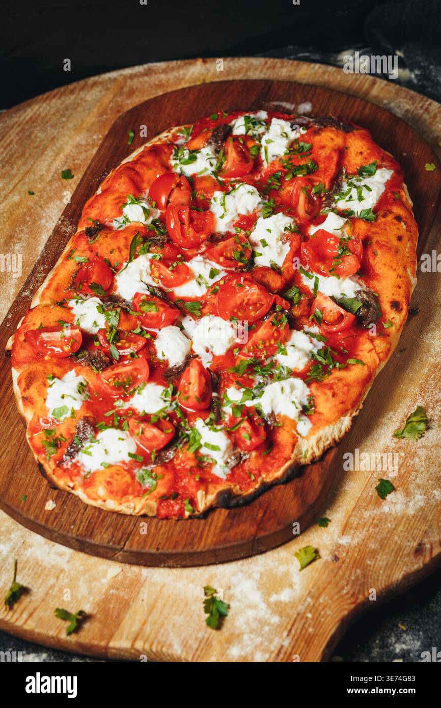 Pinsa romana italienne traditionnelle garnie de sauce tomate fraîche, de fromage mozzarella crémeux et de tomates cerises juteuses sur une planche de bois rustique. Banque D'Images