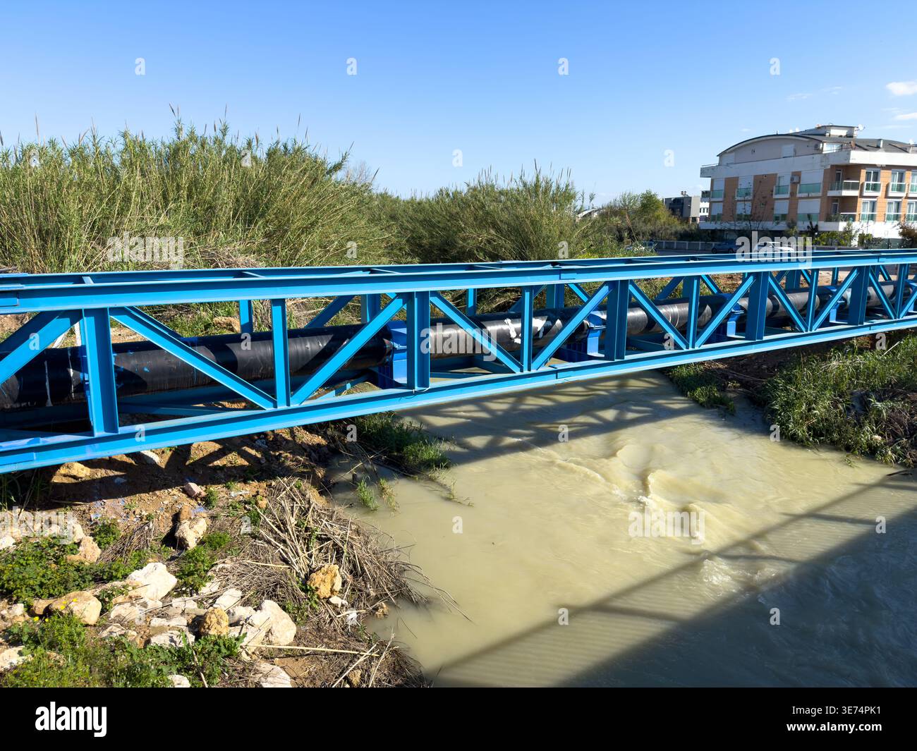 Pont en treillis d'acier bleu soutenant un grand pipeline industriel au-dessus d'une rivière qui coule Banque D'Images