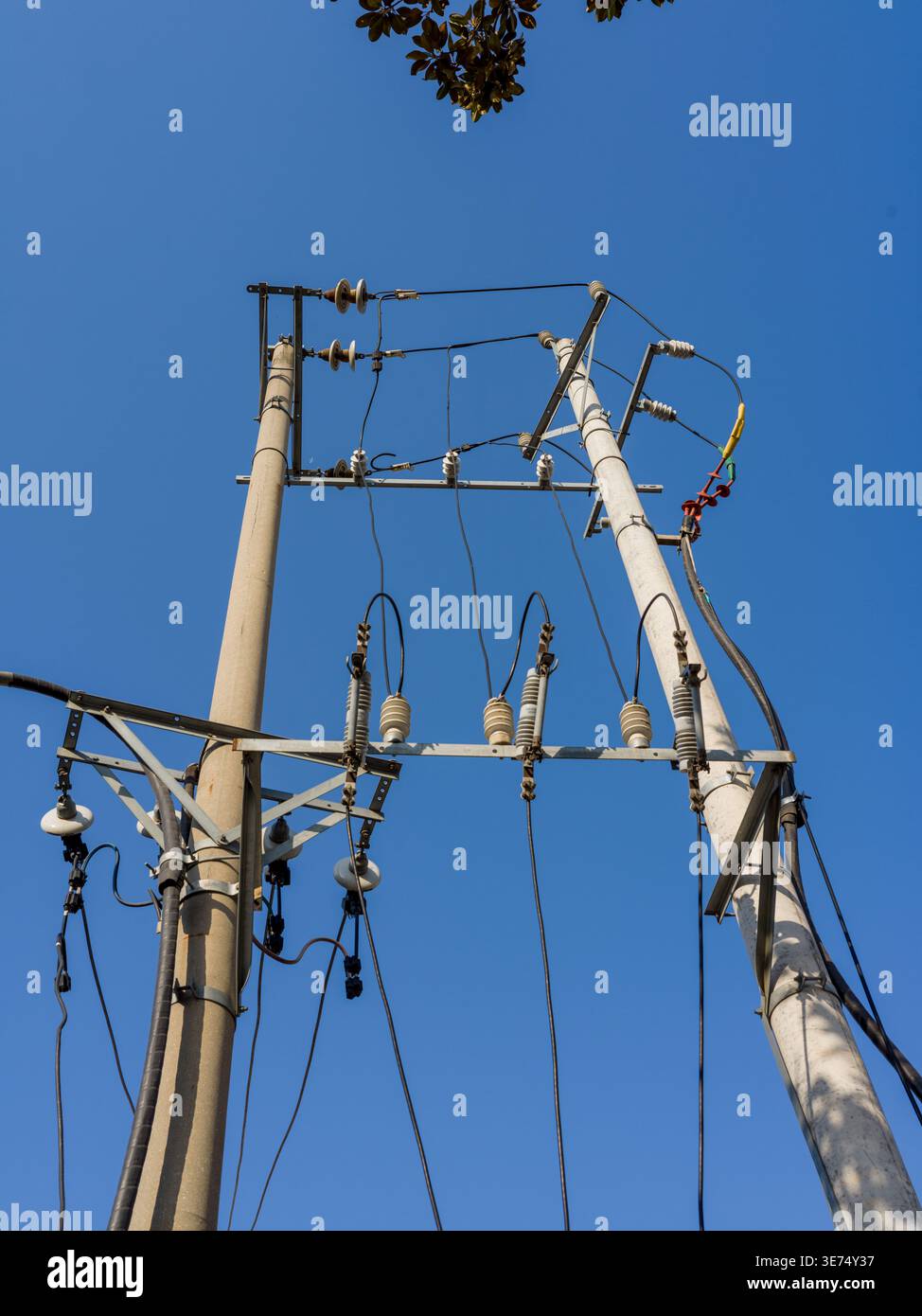 Une vue en angle bas d'un poteau électrique en béton haut supportant un réseau complexe de fils électriques noirs et d'isolants en céramique sous un ciel bleu clair. Banque D'Images