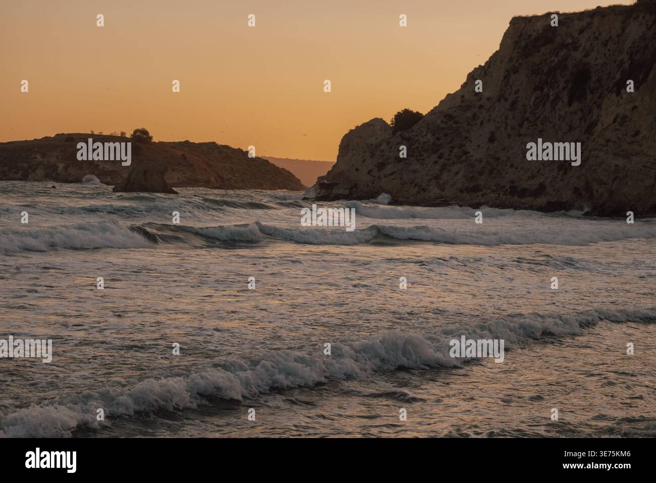 plage de galets rocheux au premier plan avec de douces vagues océaniques approchant d'énormes falaises pendant l'heure dorée Banque D'Images