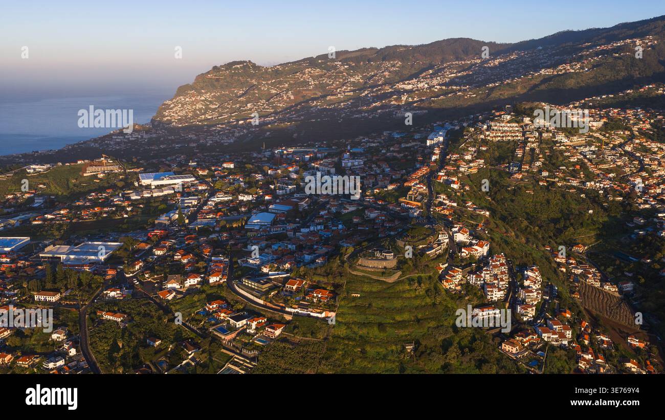 Ville en terrasses à flanc de colline à Funchal, Madère, Portugal, avec des maisons blanches et des toits rouges, océan Atlantique à gauche, routes sinueuses, clochers d'église, et long Banque D'Images
