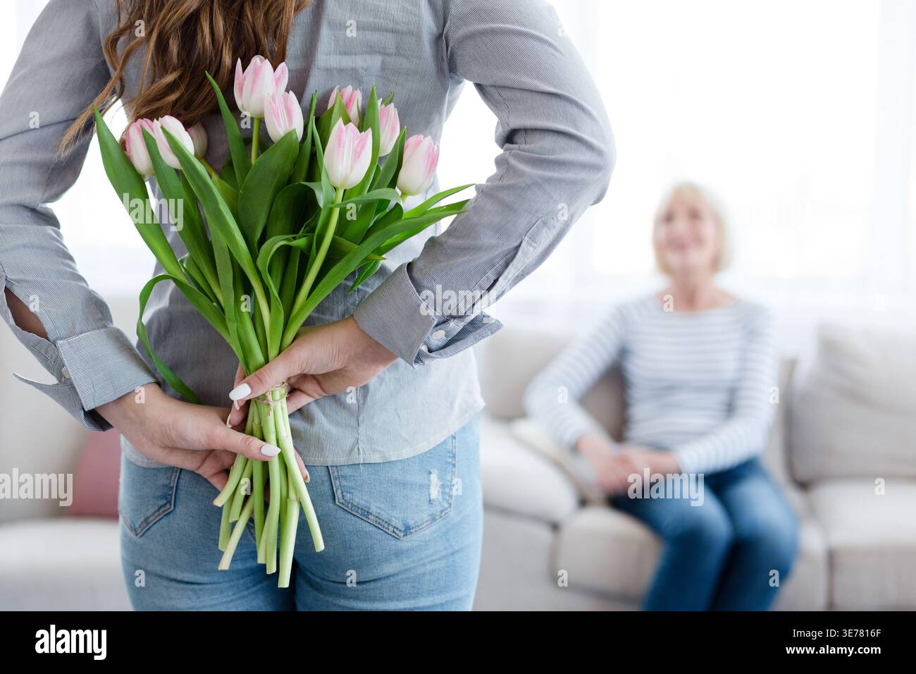 Jeune femme tenant des fleurs derrière le dos pour sa mère Banque D'Images