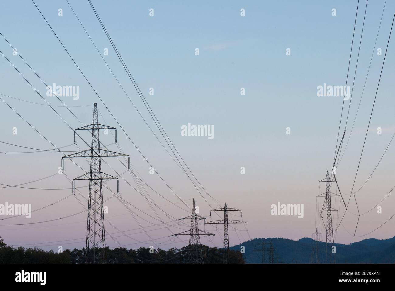 Les lignes électriques et les tours de transmission se dressent face à un ciel changeant montrant le besoin en électricité et en sources d'énergie durables. Banque D'Images
