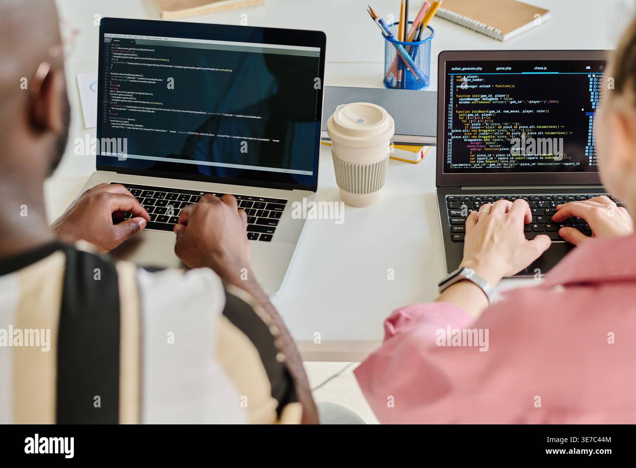 Programmeurs noirs masculins et féminins caucasiens tapant des codes de sécurité sur des ordinateurs portables tout en étant assis ensemble à table dans le bureau Banque D'Images