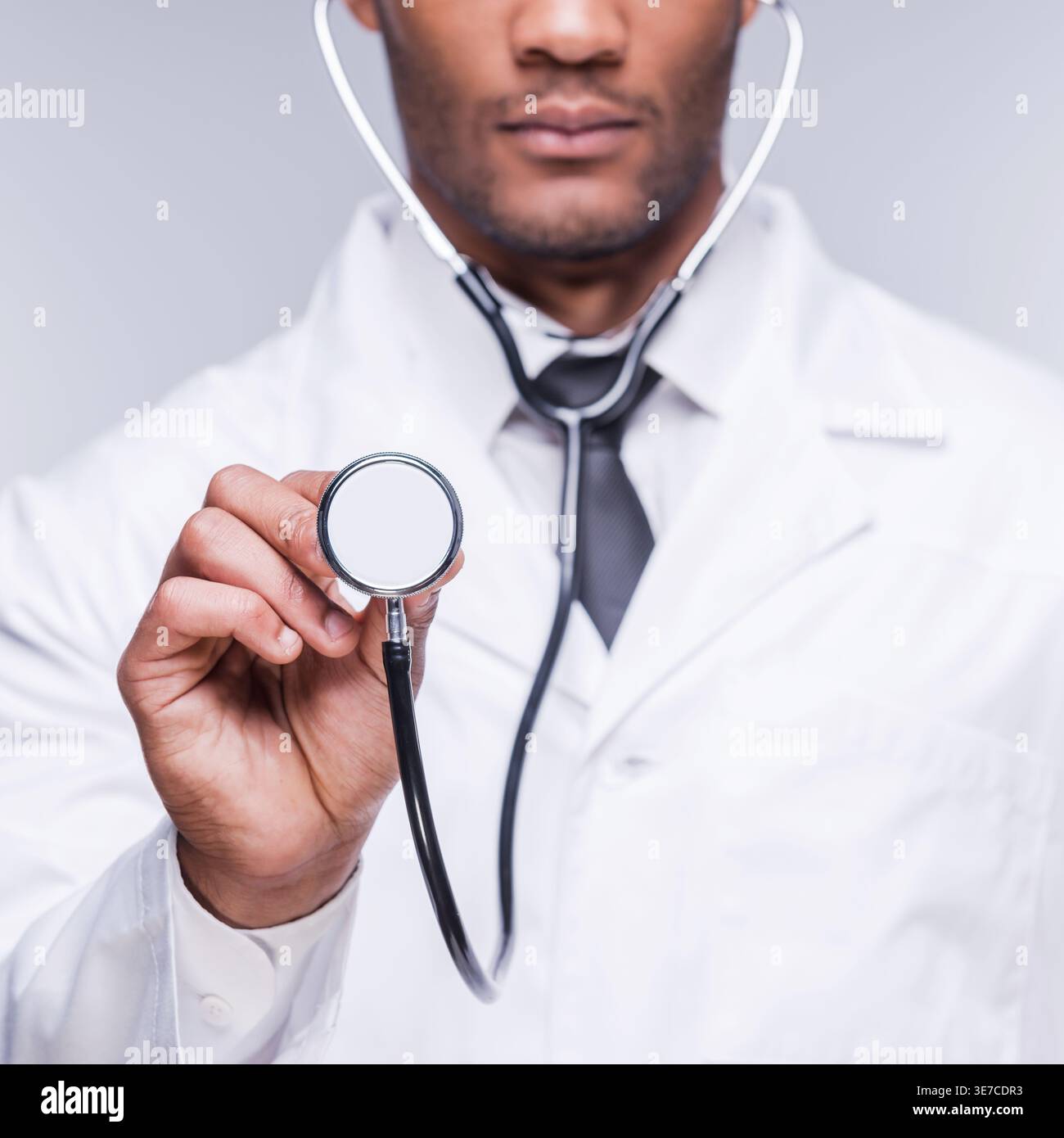 Docteur noir portant et montrant le stéthoscope tout en se tenant debout sur fond gris en studio Banque D'Images
