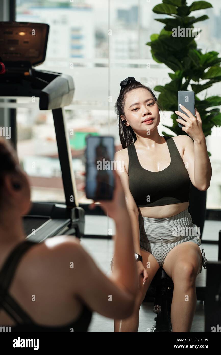 Femme asiatique prenant selfie avec smartphone assis devant le miroir dans le gymnase Banque D'Images