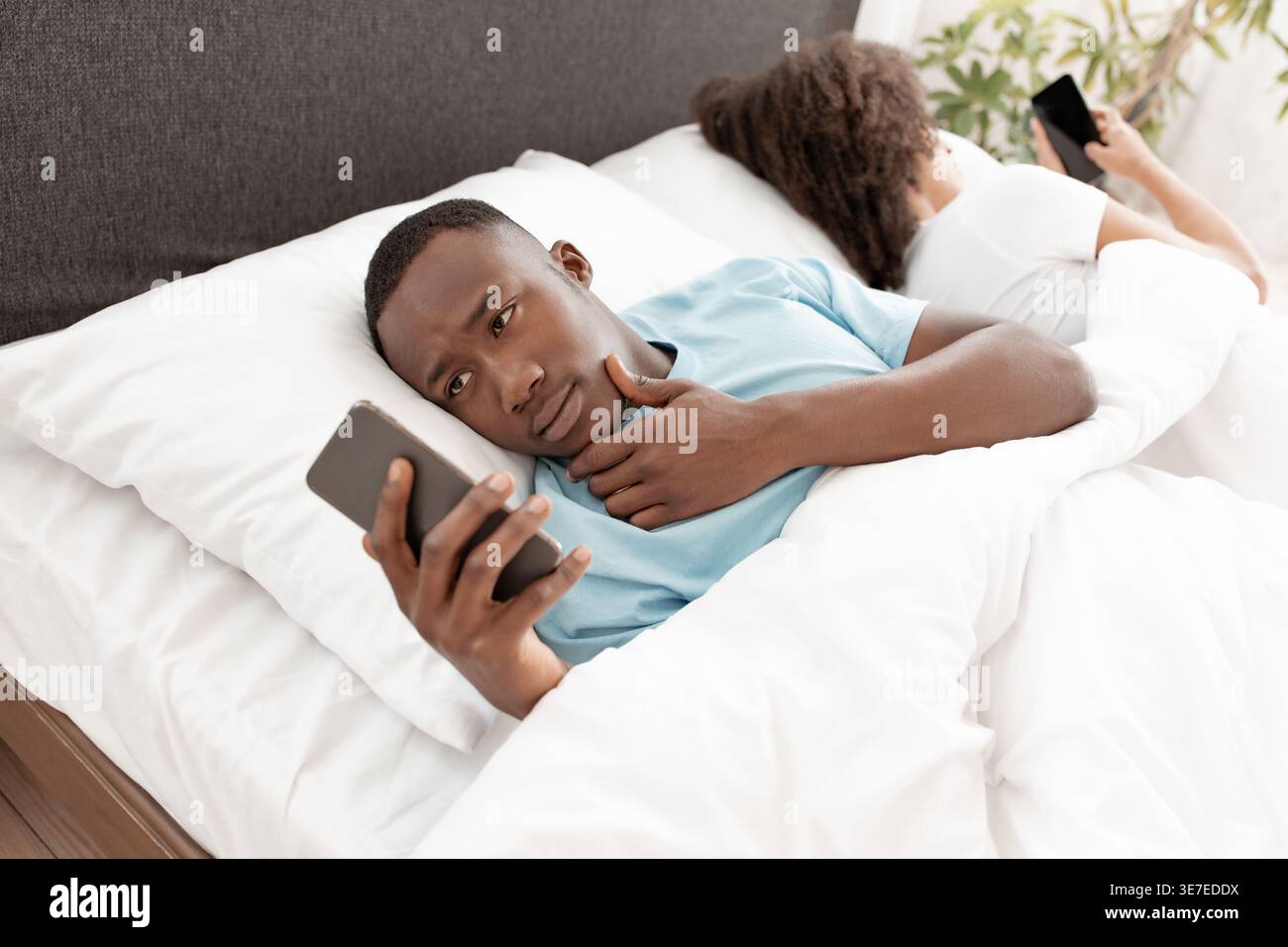 Homme noir utilisant un smartphone tout en étant allongé sur le lit contre sa petite amie dans la chambre à coucher à la maison Banque D'Images