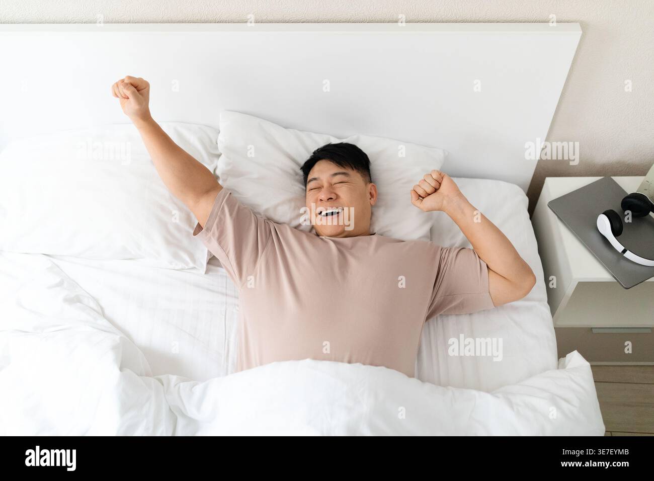 Homme asiatique étirant les bras après s'être réveillé tout en étant allongé sur le lit dans la chambre à coucher à la maison Banque D'Images